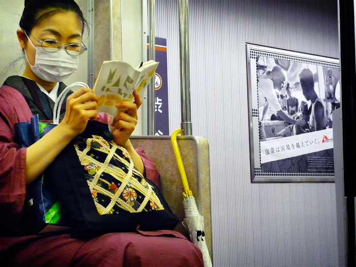 Una japonesa vestida a la manera tradicional llegint un llibre al metro de Tokyo