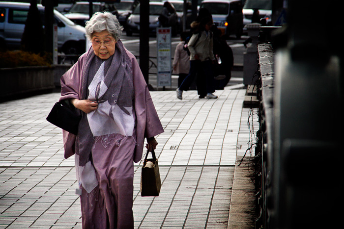 Una senyora japonesa d'edat avançada, amb el cabell gris i vestida de manera clàssica, caminant pel centre de Tokyo