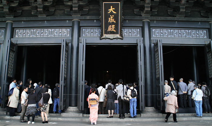 Gent a l'entrada d'un temple sintoista, mirant cap a l'interior on tot és fosc