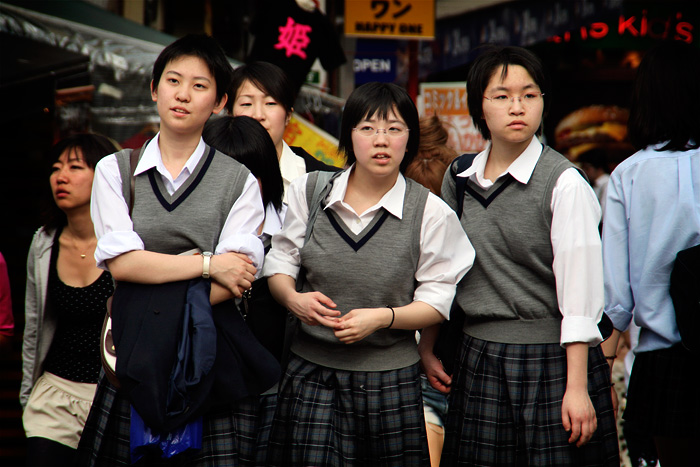 3 adolescents japoneses, vestides amb l'uniforme de l'escola: armilla de color gris, camisa blanca i  faldilla de quadres de tons grisos.