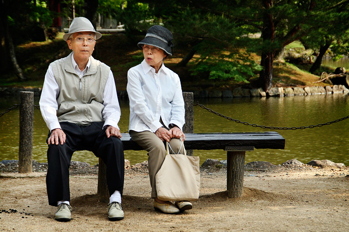 Un matrimoni d'avis japonesos, asseguts en un banc d'esquenes a un petit llac. Ell sembla sorprès i ella li està dient alguna cosa. Tots dos porten barret.